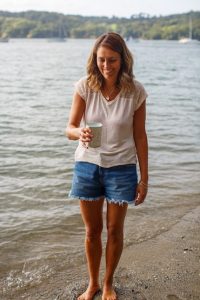 Laura Polley is stood on the shoreline wearing shorts and t-shirt holding a can of seawater she had just collected.