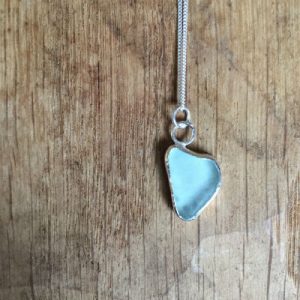 A pale blue piece of seaglass in a heart shape, set in silver to form a necklace