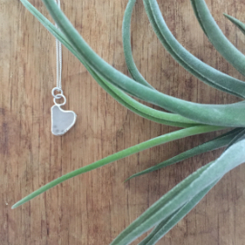 Heart-shaped white seaglass necklace set in a silver setting. 2 circular jump rings attach it to the chain.
