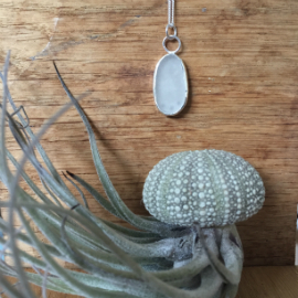 An oval white seaglass necklace with 2 circular jump rings attaching it to the chain