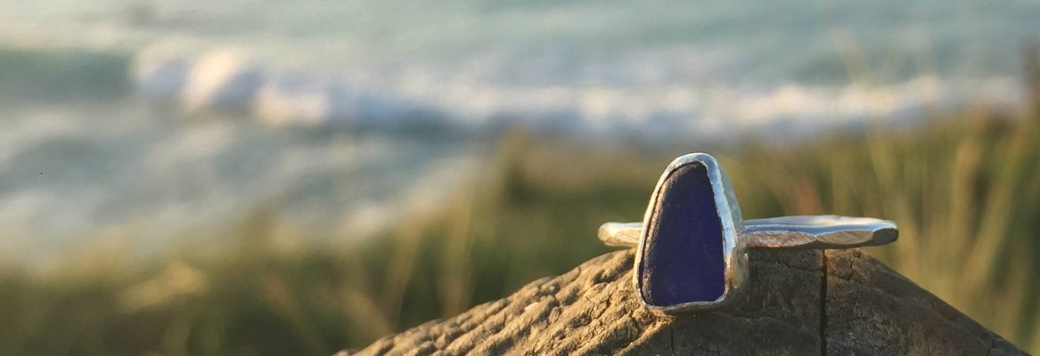Deep-blue triangle seaglass ring on a wooden post with surf in the background