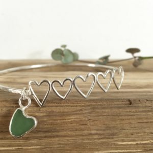Heather's commissioned bangle. 5 silver hearts (one for each dog), attached to a silver bangle, with a green heart seaglass charm.