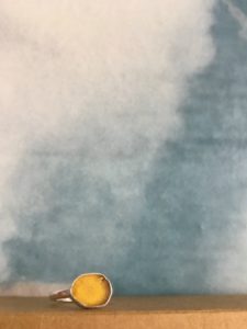 Yellow seaglass ring shown with clouds behind