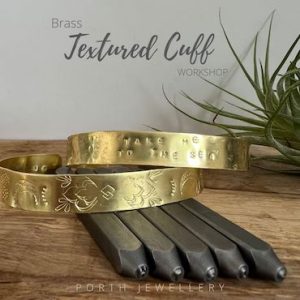 Two textured brass cuffs sit on some steel letter stamps with a plant in the right of the image.